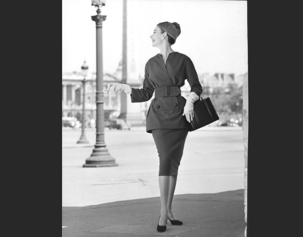 Den moderna 50-talskvinnan har välkammad knutfrisyr, pärlclips i öronen och dräkt med matchande handväska.